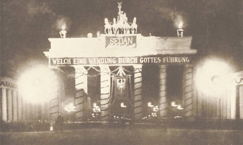 Das illuminierte Brandenburger Tor am 25. Jahrestag der Schlacht von Sedan am 2. September 1895 mit pathetischem Textbanner: “Welch eine Wendung durch Gottes Führung”.Foto: Wikipedia
